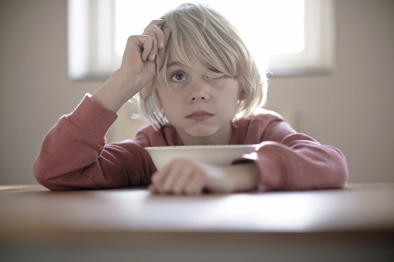 Portrait of a moody child with long blonde hair leaning over food products and looking over the cameraman's shoulder into the distance. Shot by Norwich commercial, freelance portrait photographer Matt Keal.
