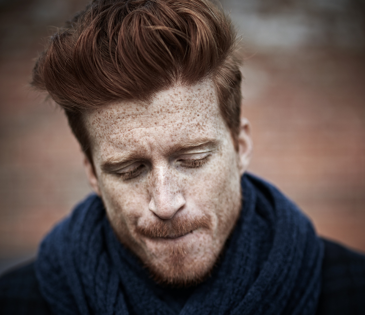 A red-haired and freckled male model looks down in this headshot. He is wearing a navy scarf for this location photoshoot. Shot by Norwich commercial, freelance portrait & product photographer Matt Keal.