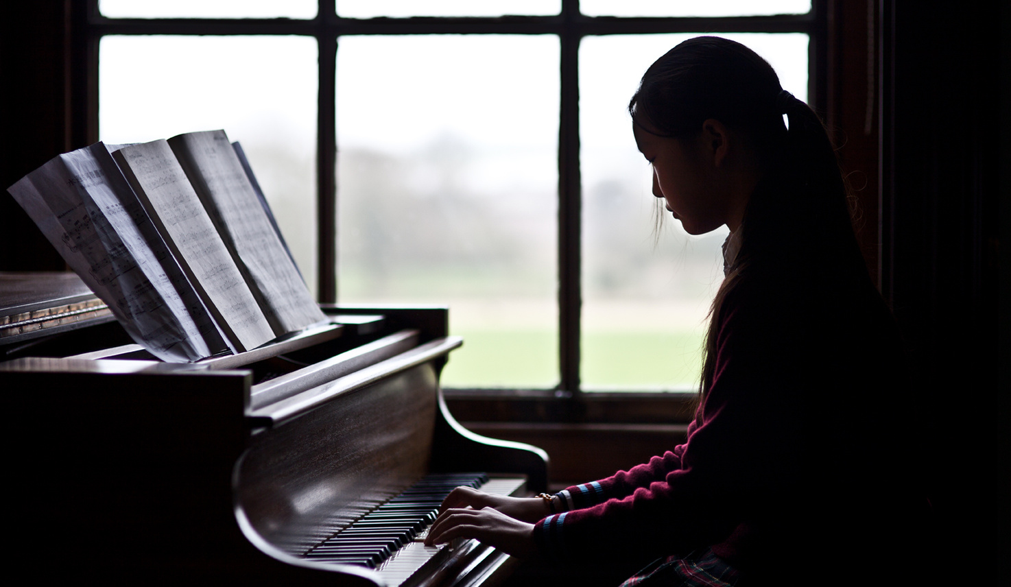 Dark and moody portrait of a young female playing the piano with sheet music. Shot by Norwich commercial, freelance portrait photographer Matt Keal.