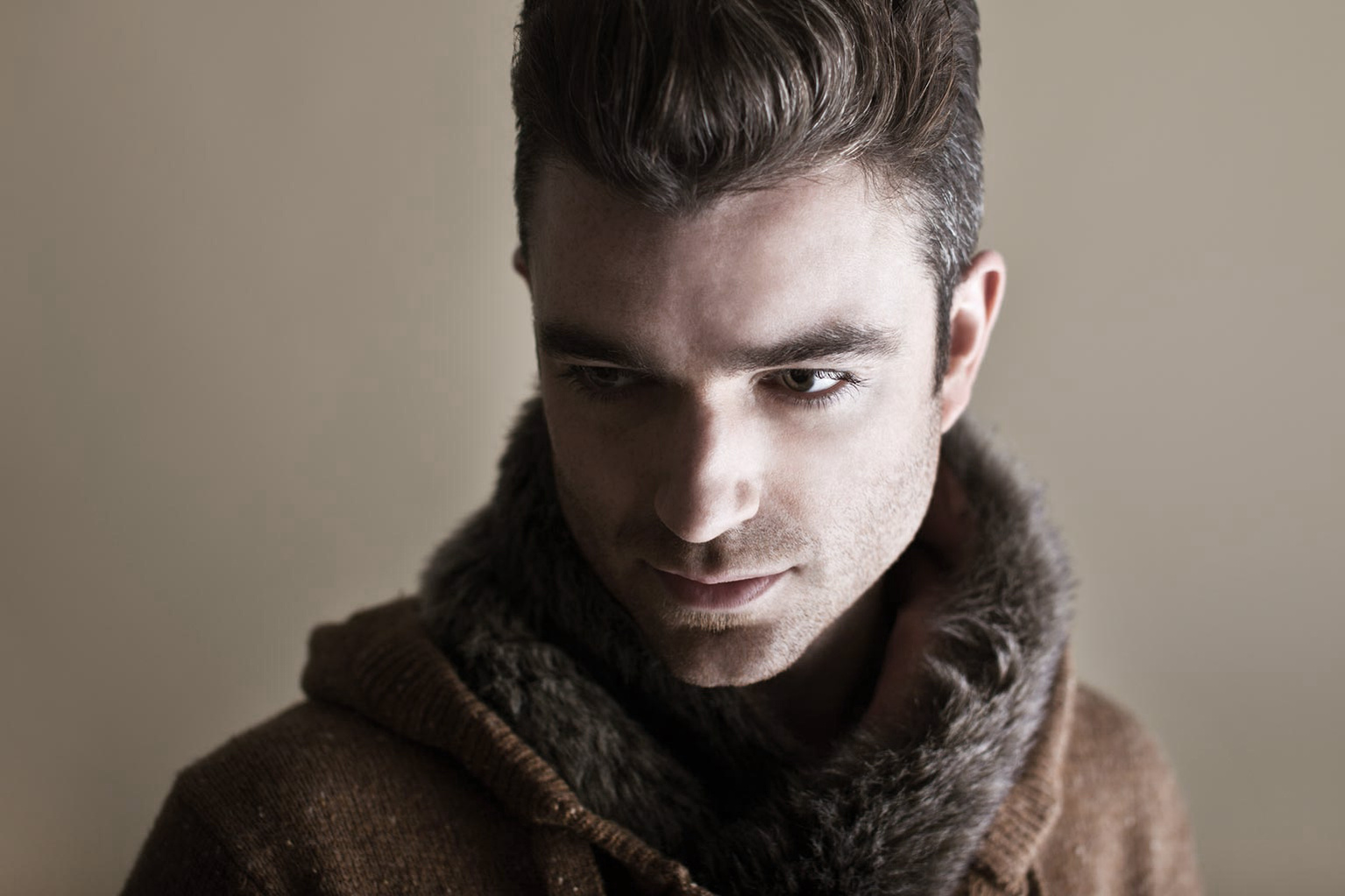 A white male model looks down and to the side in this headshot. He is wearing a fur-lined jacket for this fashion photoshoot. Shot by Norwich commercial, freelance portrait photographer Matt Keal.