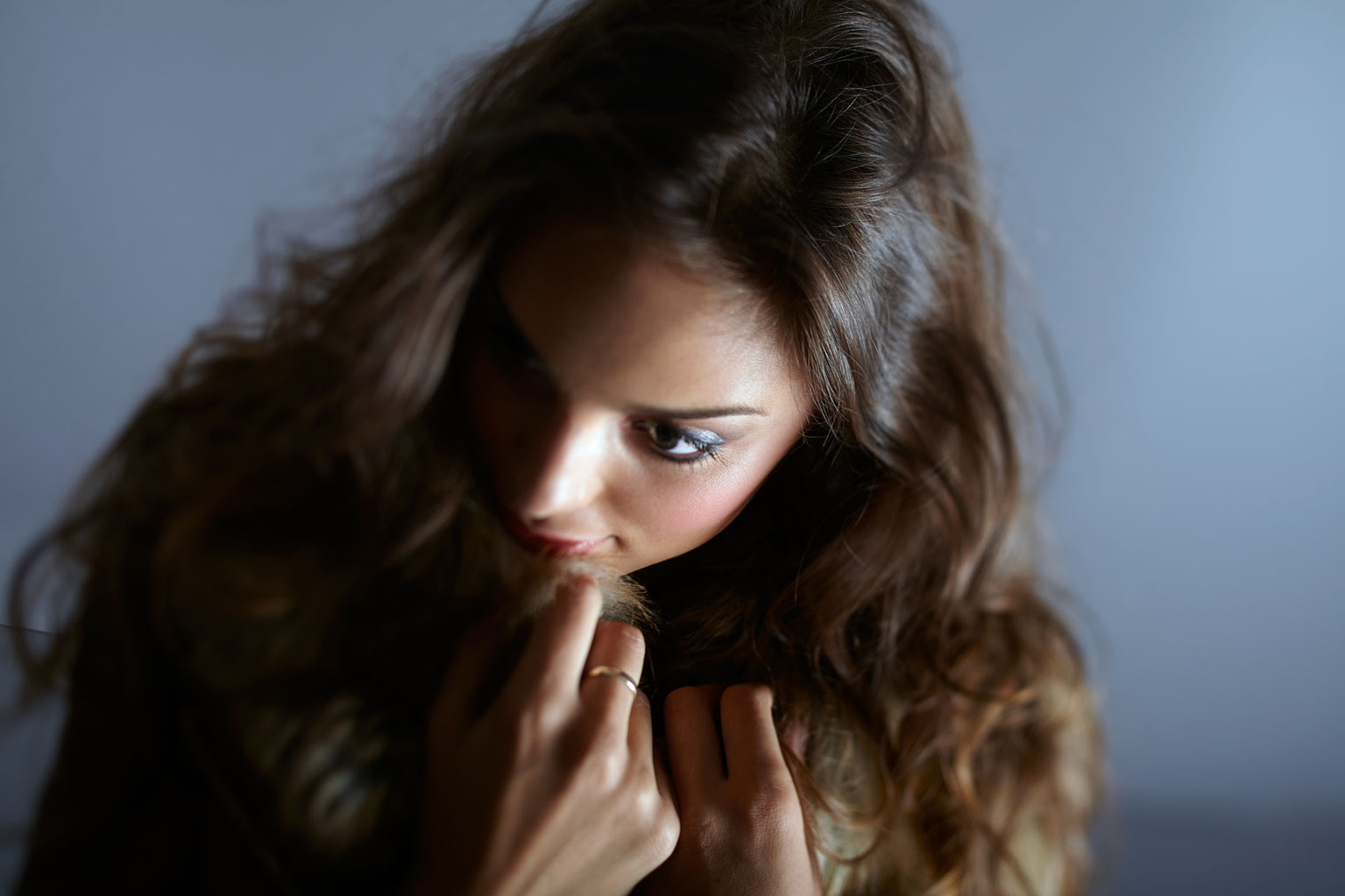 A female model looking down and pulling her coat up to her face for a fashion campaign. Shot by Norwich commercial, freelance portrait photographer Matt Keal.