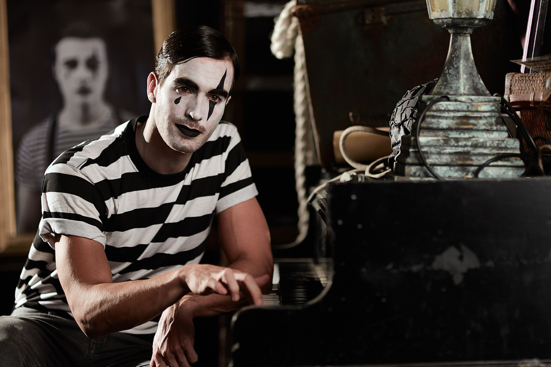 Wide angle portrait shot of a male model wearing clown face paint and a striped t-shirt and playing the piano. Shot by Norwich commercial, freelance portrait photographer Matt Keal.
