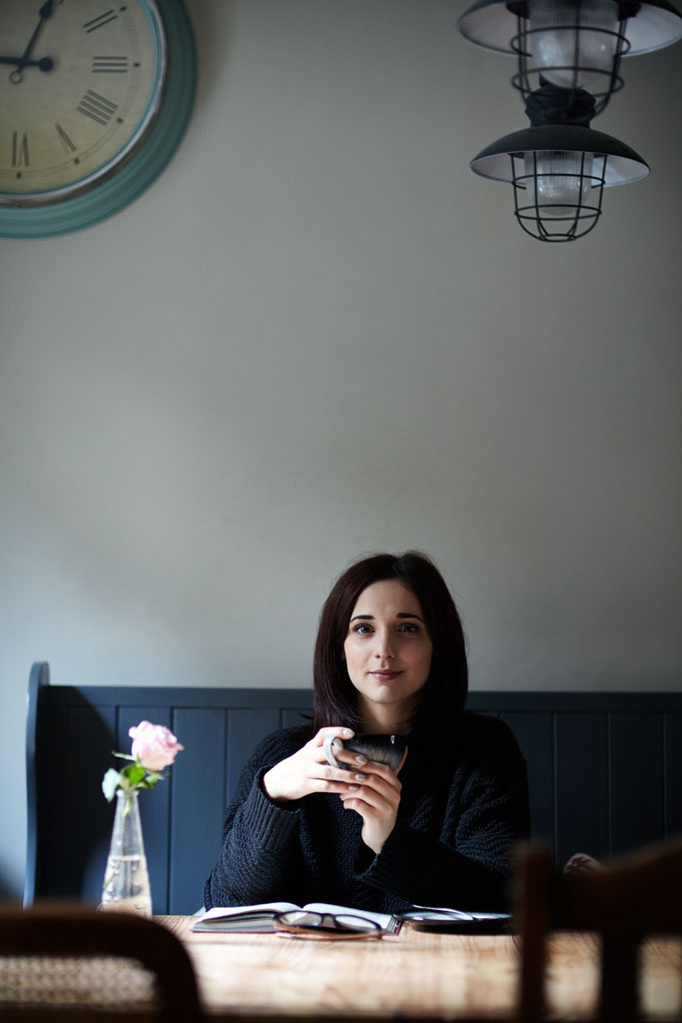 Headshot of a female entrepreneur drinking a coffee in a cafe with her notebook and glasses on the table. Shot by Norwich commercial portrait photographer Matt Keal.