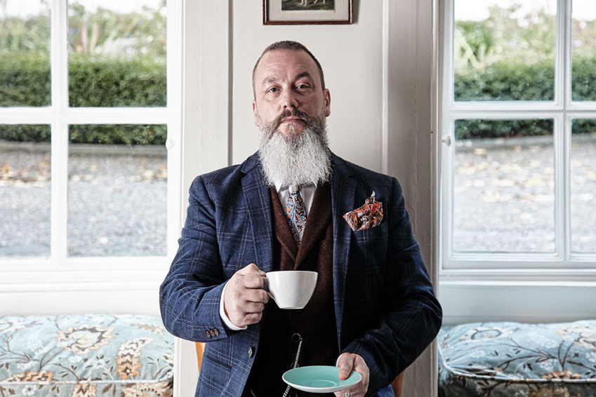 Portrait of a bearded man in a formal suit holding a cup & saucer in a wedding venue. Shot by Norwich commercial, freelance portrait photographer Matt Keal.