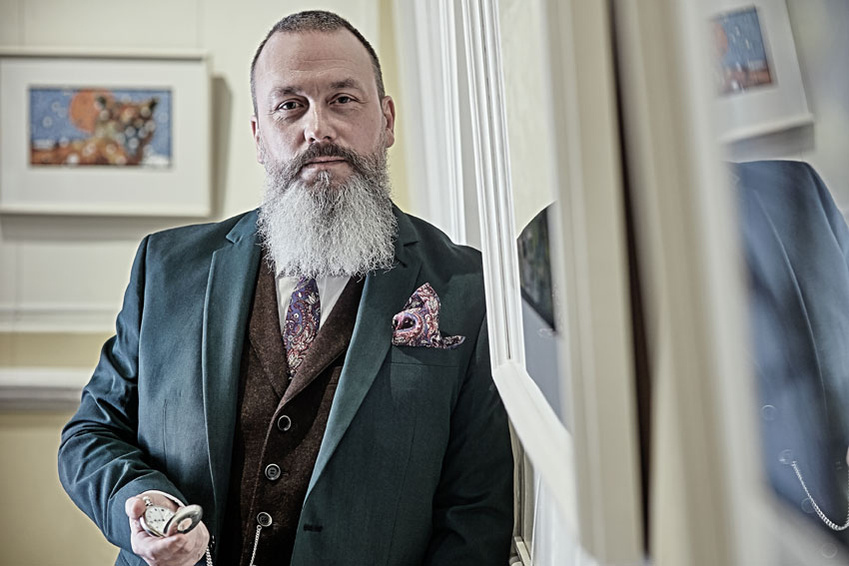Portrait of a bearded business owner holding a pocket watch and leaning against the wall. Shot by Norwich commercial, freelance portrait photographer Matt Keal.
