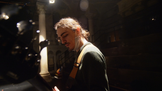 a bassist is looking down at his instrument and is playing, the light from above is lighting his hair