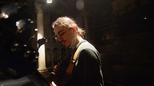 a bassist is looking down at his instrument and is playing, the light from above is lighting his hair