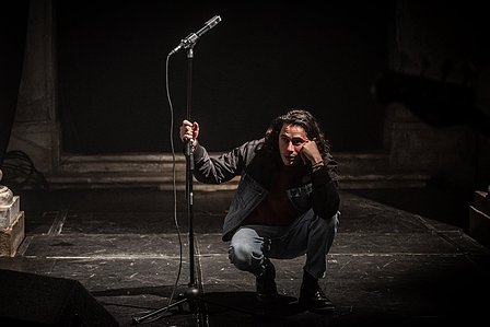 A man squatting is close to a microphone waiting to sing