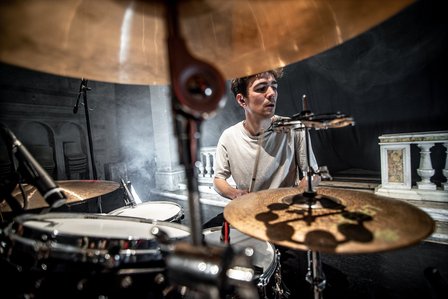 A man sits in front of a drum and is about to play it.