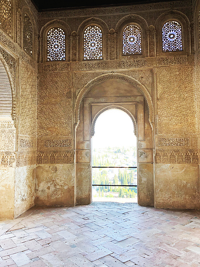 Large interior space of a Church with sturdy concrete walls, round archways and four, small, colourful mosaic windows 