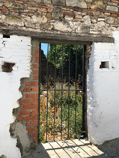 External, black metal gate nestled between white walls showing exposed brick underneath