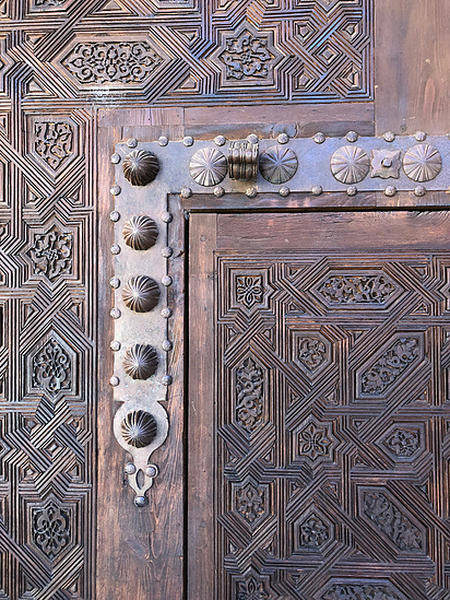 Intricate pattern on a large wooden exterior door with decorative metal bolts