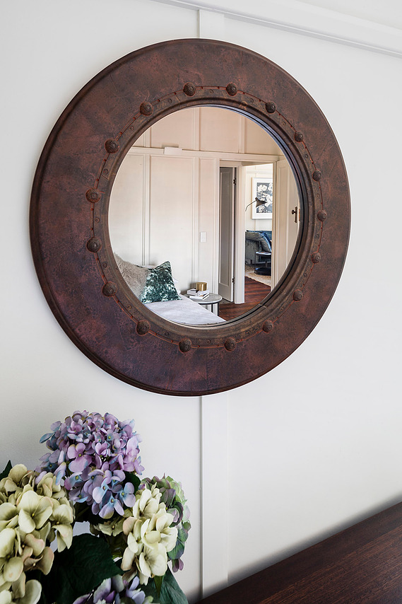 Rustic mirror with faux metal bolts on a white wall in the bedroom 