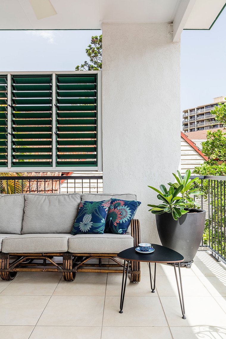Apartment balcony with grey couch, black side table and green plant in a big black pot 