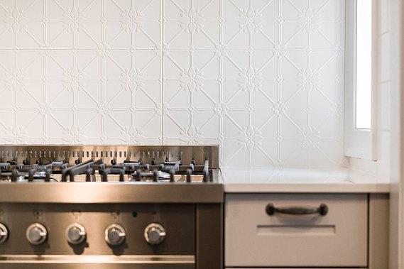 Stainless steel, gas cooktop with a white, patterned wall behind