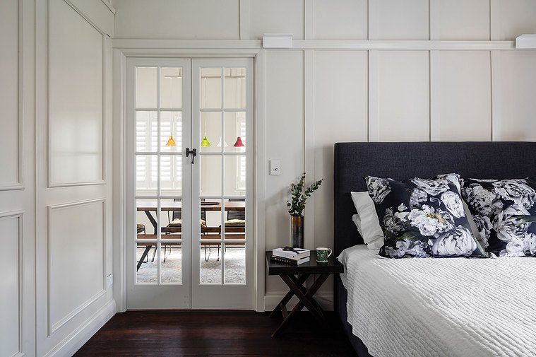 White bed decor with black headboard and side table, looking out onto the dining room through a glass door