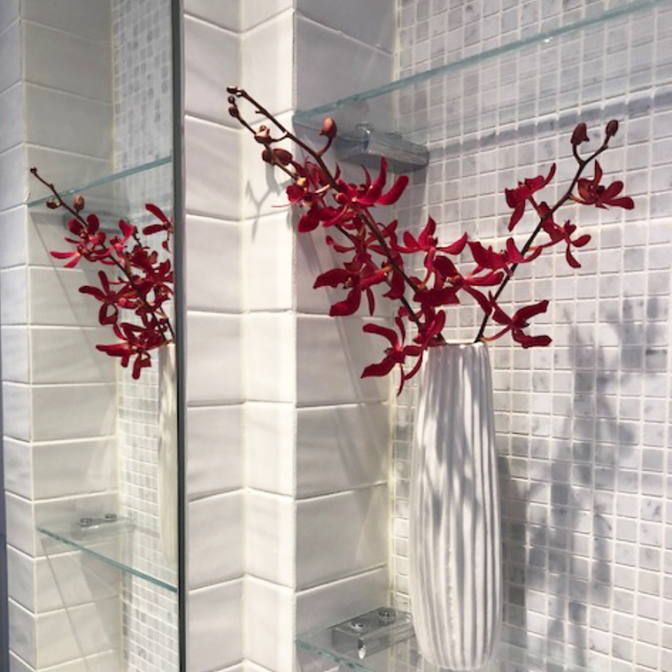 Red plant in a white vase in a bathroom with small white tiles lining the walls