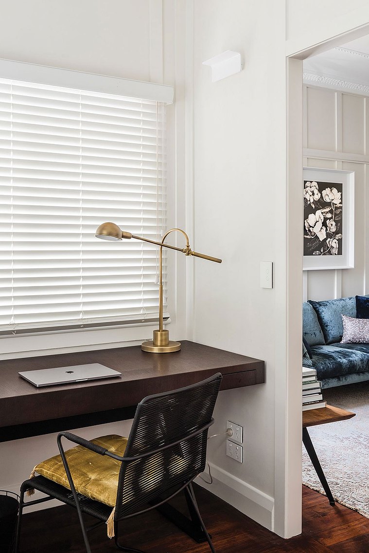 White office with dark wooden desk and black and gold desk chair with a view of the living room