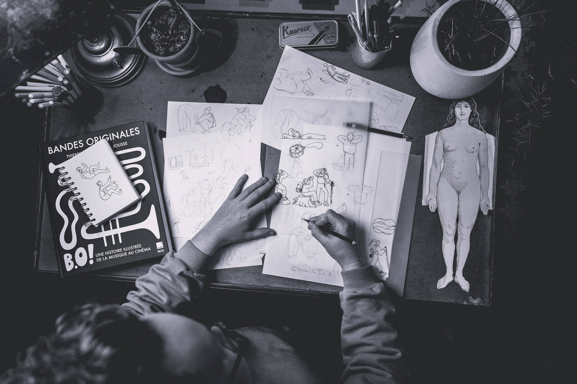 Photo of artist Clemence Thune at her desk, creating sketches for an illustration on the theme of the pleasure of being together in a natural environment.