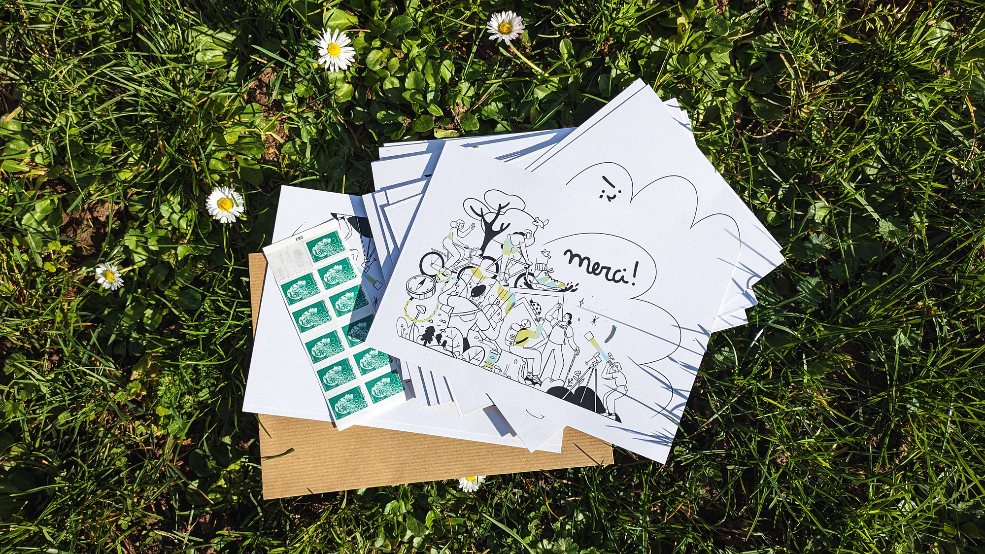 Photo of the postcards created. They are displayed outside on the grass. We can see French stamps next to them.