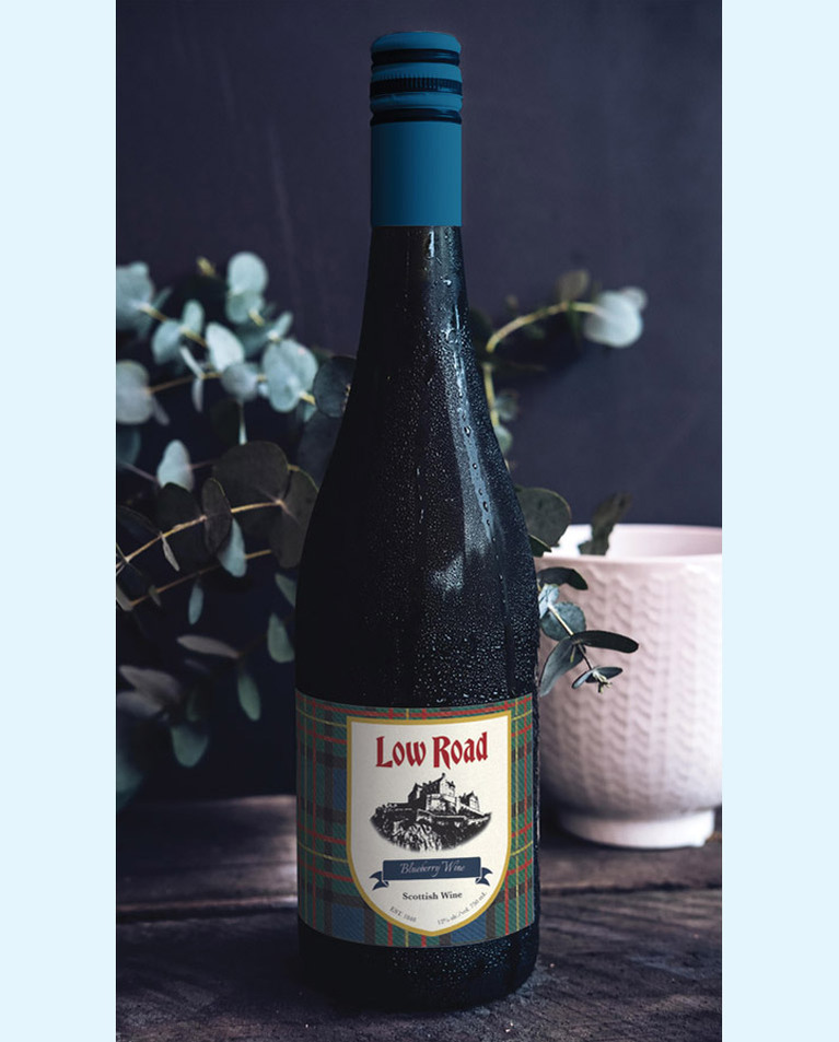 Label on wine bottle. It has a blue tartan pattern background with a shield in the canter containing the Low Road logo and wordmark.