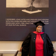 A HBS graduate in cup and gown posing inside Baker library, Boston, MA