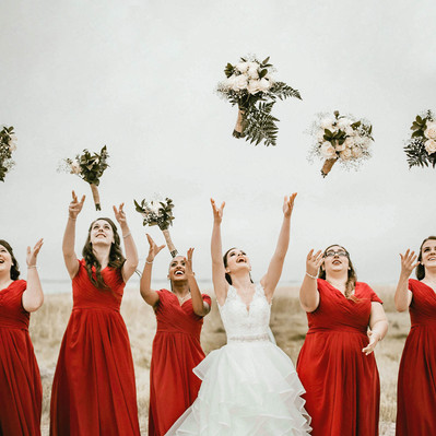 A bride with bridesmaids are throwing their bouquets in the air on the beach. Photographer Ivan Djikaev/Mind On Photography.