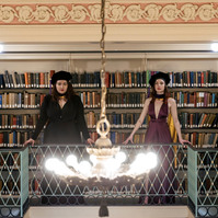 Two women in cups and gowns posing in a library for graduation portrait