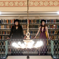 Two women in cups and gowns posing in a library for graduation portrait