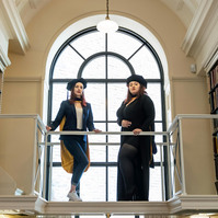 Two women, graduating from Suffolk University, posing on a balcony
