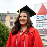 A BU graduate wearing cup and gown in front of famous Citgo sign in Boston.