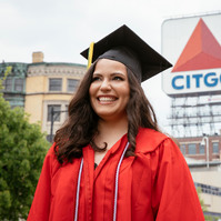 A BU graduate wearing cup and gown in front of famous Citgo sign in Boston.