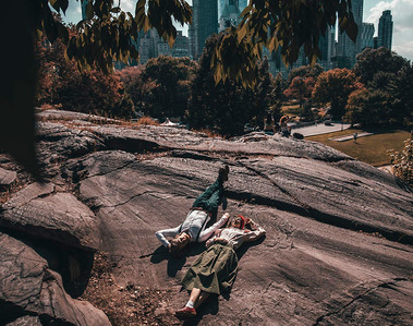 A newly engaged couple is lying on rocks in Central Park, NYC. Photography by Ivan Djikaev/Mind On Photography