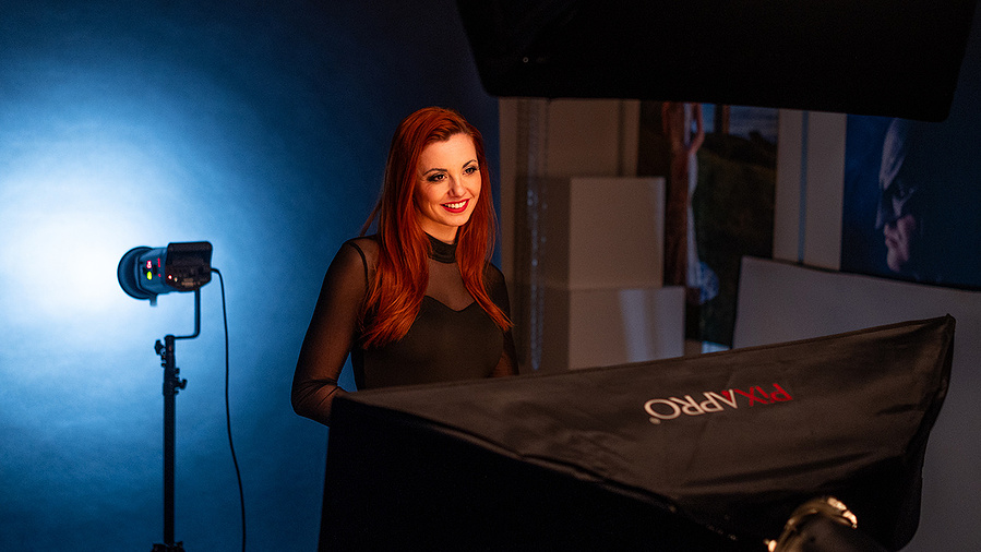 Female model Hannah wearing a black sheer top and smiling at the camera, in a studio with spotlight on 