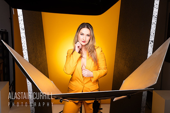 Female model wearing a yellow suit looking directly into the camera with yellow backdrop and studio lighting 