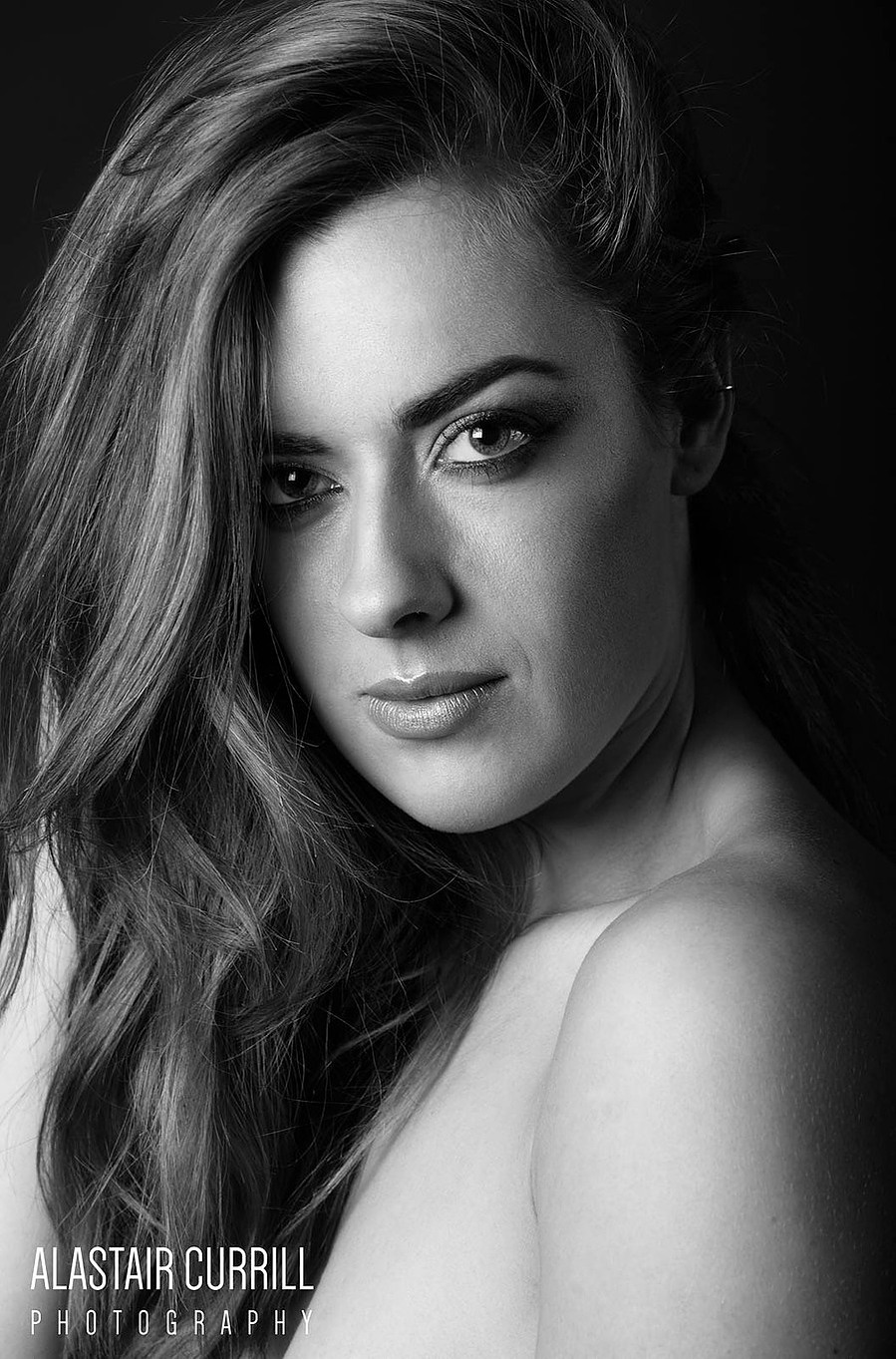 female model headshot pose in black and white, long loose hair flowing over bare shoulders