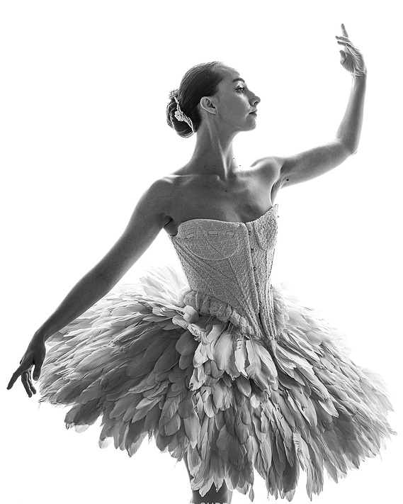 Female model Erica posing in a ballet stance, wearing a corset top with feathered skirt against a white backdrop 