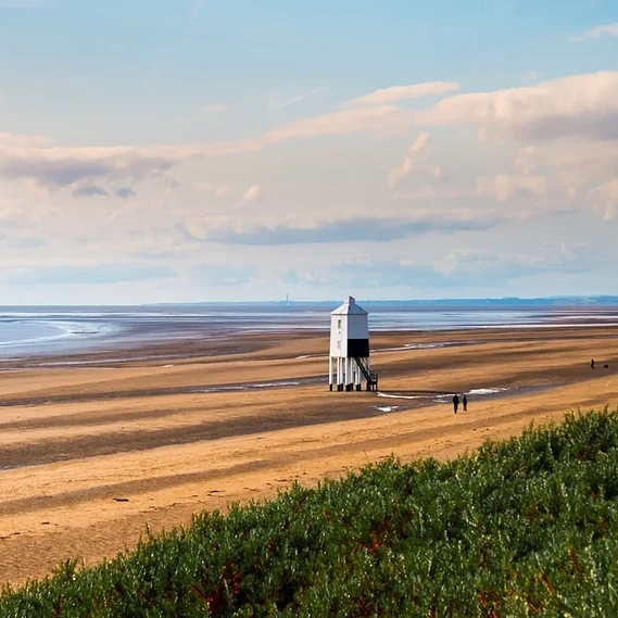 Beach seascape of Burnham on sea with golden sand, pale blue sea and blue sky with white clouds, lighthouse in the distance 