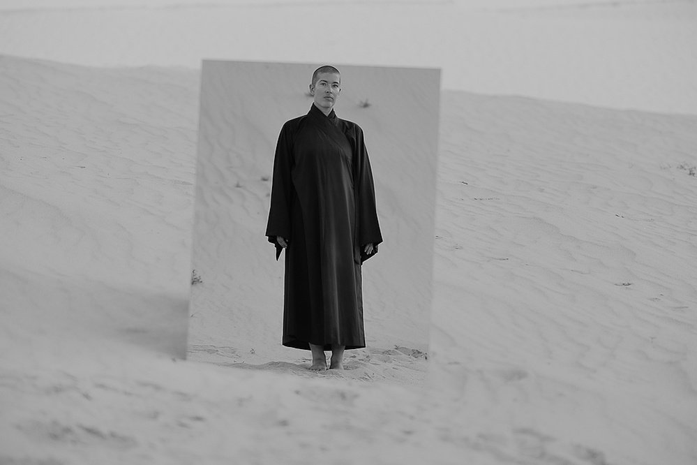 a buddhist monk in a red robe photographed by Cari Faye Antonovich of The White Room Studios at the Seminoe sand dunes near Rawlins Wyoming at sunset with a mirror
