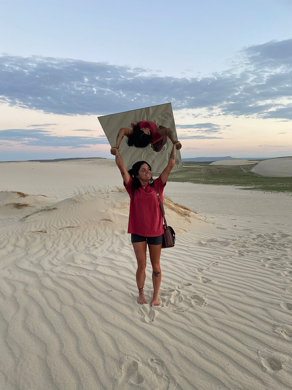 behind the scenes photo of a portrait session with Cari Faye photography at the Seminole sand dunes in Wyoming. Cari Faye Antonovich is photographed here holding a giant mirror above her head