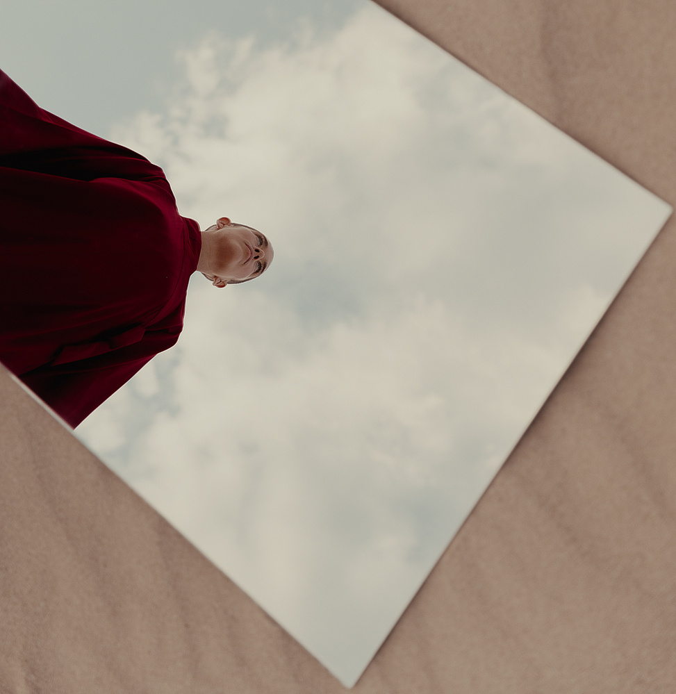 a buddhist monk in a red robe photographed by Cari Faye Antonovich of The White Room Studios at the Seminoe sand dunes near Rawlins Wyoming at sunset with a mirror