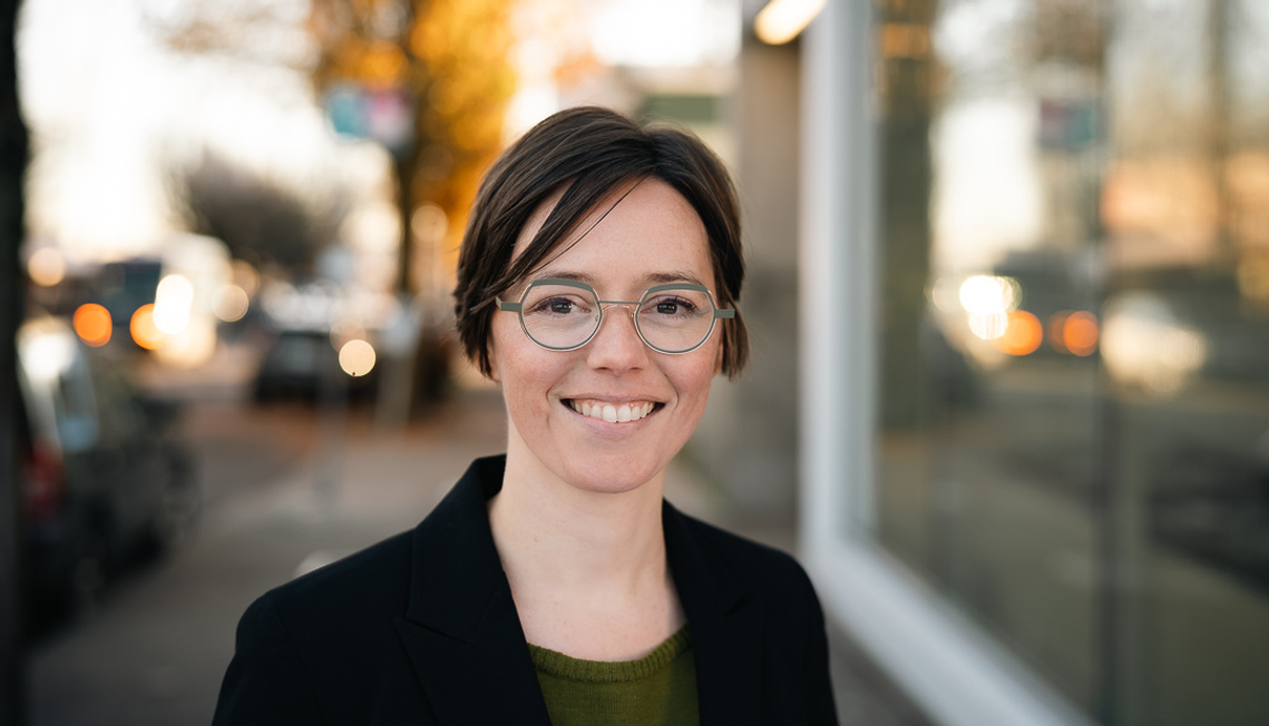 Headshot of a young white woman smiling and wearing a business jacket in the street