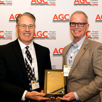 Two formally dressed white men stand in front of a step and repeat, receiving an award at the 2025 Associated General Contractors annual conference