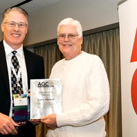 Two formally dressed white men stand in front of a step and repeat, receiving an award at the 2025 Associated General Contractors annual conference