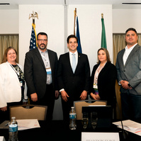 A group of business people stand in front of flags in a board room