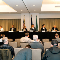 A board room full of people, being addressed by the board of directors