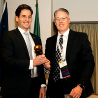 Two men exchange a gavel, indicating the changing of presidents for the 2025 AGC (Associated General Contractors) conference