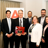 A group of people stand in front of a "step and repeat", receiving an award