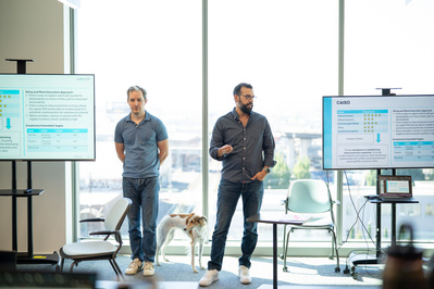 Two men in front of large office windows giving a presentation