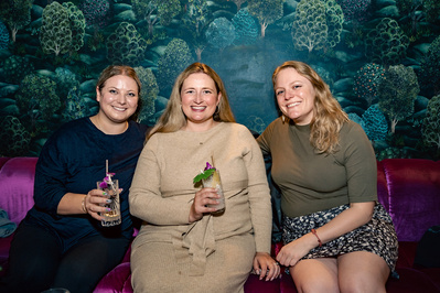 Three women sitting together and having a drink in a moodily lit room